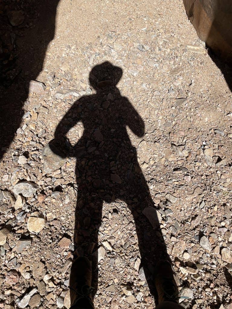 Shadow of a Belinda by herself wearing a hat, on the Larapinta Trail, cast on rocky ground with sunlight creating distinct edges.