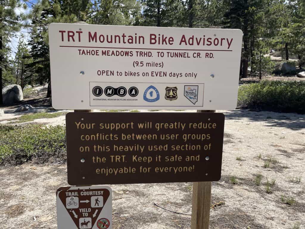 Sign in a wooded area indicating TRT Mountain Bike Advisory, Tahoe Meadows to Tunnel Creek Road. Biking allowed on even days only. Reminder to yield to hikers displayed below. Follow the principles of Leave No Trace to preserve this beautiful environment.