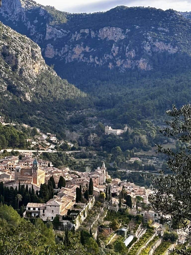 A picturesque village with stone buildings nestled in a valley, surrounded by dense forests and mountains, is perfectly situated along the GR221 dry stone route in Mallorca.