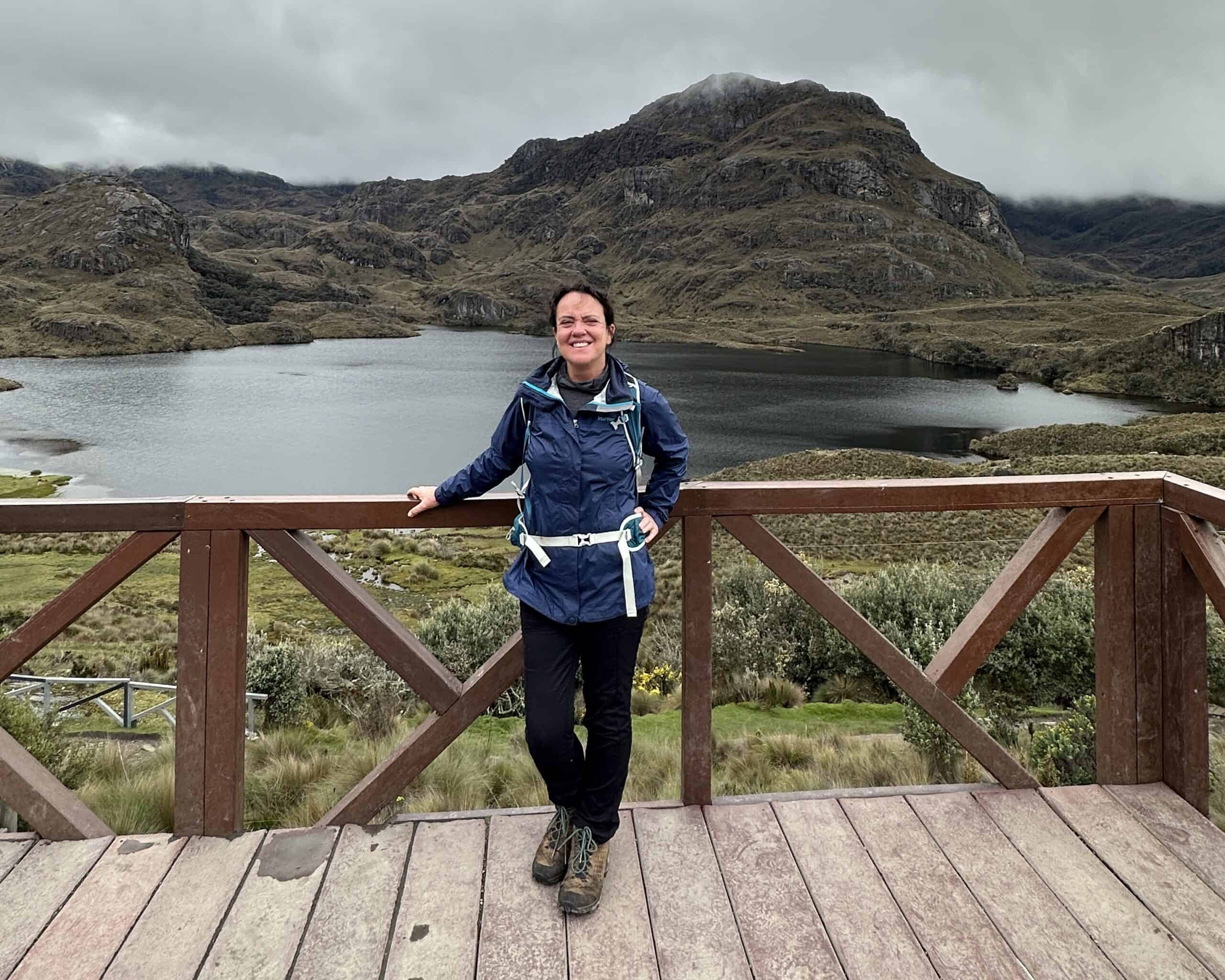 Woman in blue rain jacket wearing day pack and standing in front of Lake in Cajas National Park Ecuador