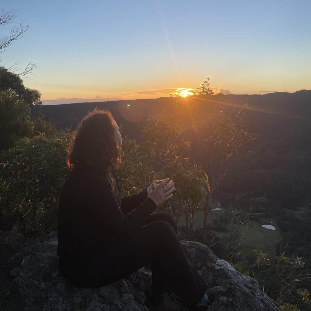 Woman sitting on the ledge drinking a cup of coffee watching the sunrise on a hiking Trail eating food for day hikes