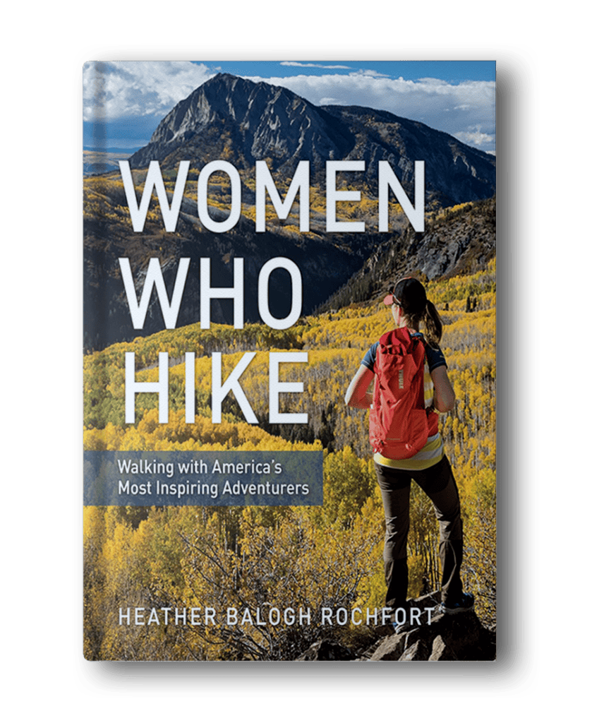 Cover of the book "Women Who Hike" by Heather Balogh Rochfort, depicting a woman with a red backpack hiking in a mountainous area with autumn foliage. This is one of the must-have hiking books for women seeking inspiration and adventure.