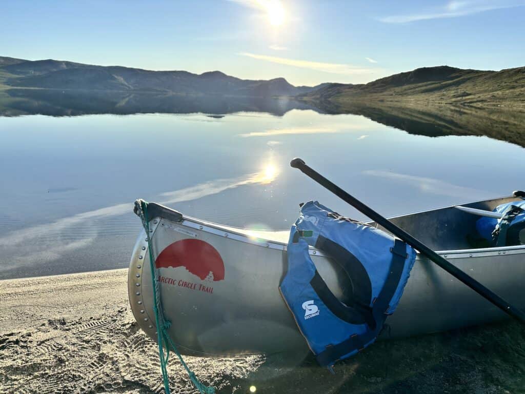 metal canoe with Arctic Circle Trail logo written on it and a blue lifejacket outside a lake