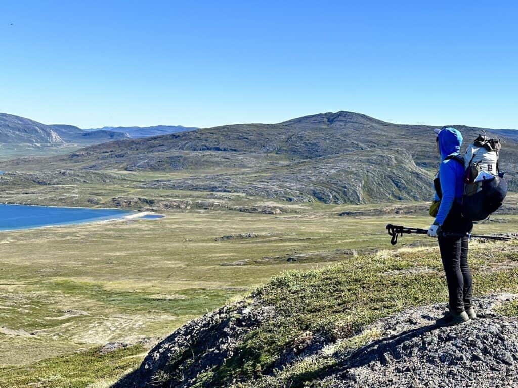 Belinda in a blue sun hoodie looks out over a valley and green hills to a blue lake