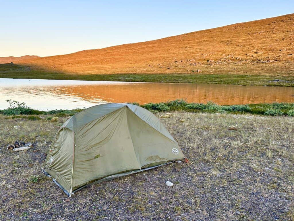 green tent is pitched on the shores of a lake - under the midnight sun glow on the Arctic Circle Trail