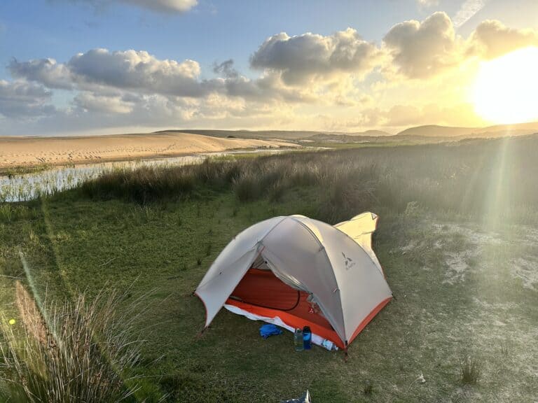 white tent on grassy verge beachside with sand dunes in background.